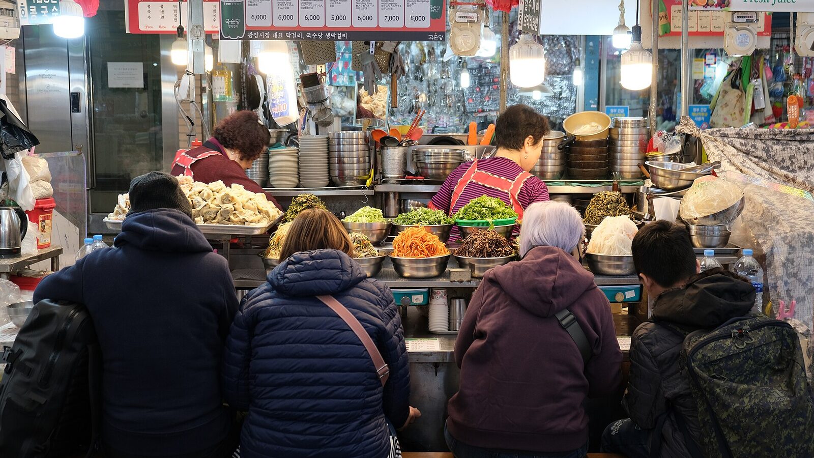 Locals shoulder to shoulder at a market food counter, eating where the cooking happens